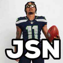 a man in a seahawks jersey holds a football in front of a sign that says json