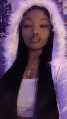 a woman with long black hair is wearing a white fur hooded jacket and a cross necklace .