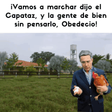 a man in a suit is holding a chicken in front of a sign that says vamos a marchar