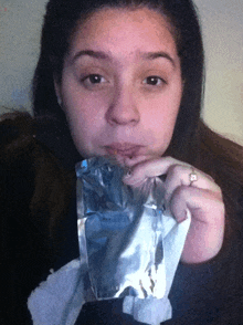 a woman eating a piece of aluminum foil with a ring on her finger