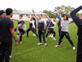 a group of men are stretching on a field and one of them is wearing a shirt that says ' santr '