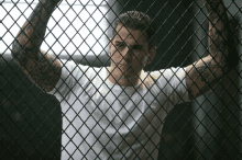 a man behind a chain link fence with a tattoo on his arm