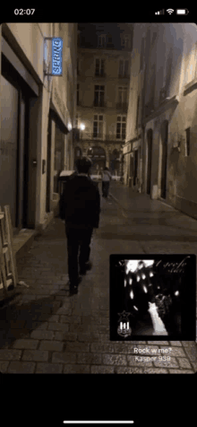 a phone screen shows a man walking down a cobblestone street with a spring store in the background