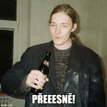 a man in a black jacket holds a bottle of beer and says " preeesne "