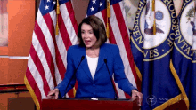 a woman in a blue jacket stands at a podium in front of a flag that says house of representatives