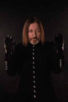 a man with long hair and a beard is wearing black gloves and a black coat