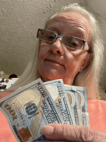 a woman wearing glasses holds a bunch of 100 dollar bills