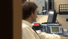 a man in a yellow shirt and tie sits at a desk in front of a telephone