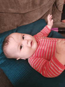 a baby in a pink and white striped shirt is laying on a blue blanket