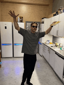 a man standing in a kitchen with his arms outstretched holding a tray of food