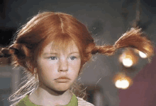 a little girl with red hair and pigtails is looking at the camera .