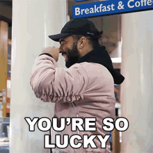 a man wearing a pink jacket and a black hat is standing in front of a sign that says breakfast & coffee