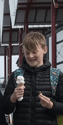 a young boy with a backpack is eating an ice cream cone and a chocolate bar