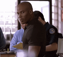 a man in a black shirt with a blue badge on his shoulder stands in front of a man in a blue shirt