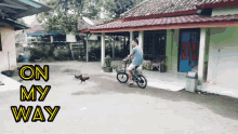 a man riding a bike in front of a house with the words " on my way " on the bottom