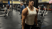 a man in a white tank top holds a dumbbell