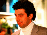 a man with curly hair is wearing a white turtleneck and a grey jacket