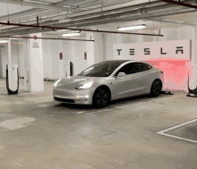 a silver tesla model 3 is parked in a tesla charging station