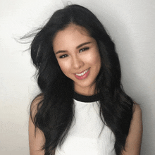 a woman with long black hair and a white top smiles for the camera