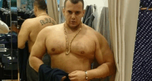 a shirtless man with a tattoo on his back is standing in a dressing room .