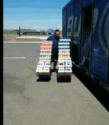 a man is carrying a stack of boxes of soda in front of a blue truck that has the letter b on it