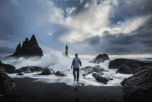 a man stands on a rocky beach looking at a stormy ocean