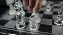 a person is playing a game of chess with clear glass chess pieces on a chess board .