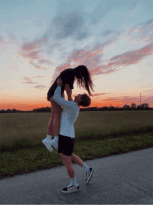 a man is holding a woman in his arms in front of a field with a sunset in the background