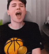 a young man wearing a black t-shirt with a basketball on it is yawning with his mouth open .
