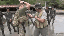 a group of soldiers are standing in a muddy area and one of them is holding another man 's arm .