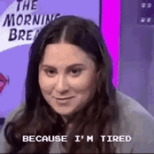 a woman is sitting in front of a sign that says `` because i 'm tired '' and smiling .