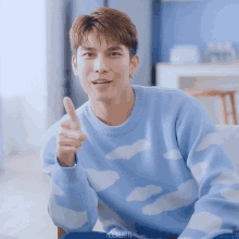 a man wearing a blue sweater with clouds on it points his finger