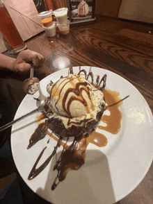 a white plate topped with a brownie with ice cream and chocolate sauce