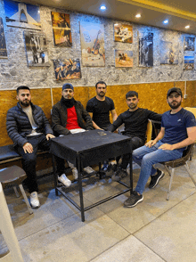 a group of men sit around a table with pictures on the wall above them