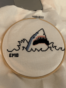 a cross stitch of a shark with the word emo written below it