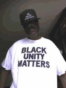 a man wearing a black hat and a white shirt that says " black unity matters "