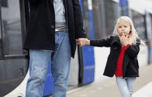 a man and a little girl are holding hands while waiting for a bus at a bus stop .