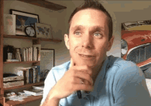 a man in a blue shirt is sitting in front of a bookshelf with a picture of a red car on the wall