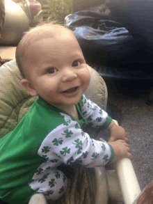 a baby wearing a green and white outfit with shamrocks on the sleeves is smiling