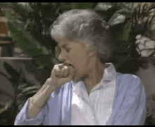 a woman with gray hair and a blue cardigan is biting her nails .
