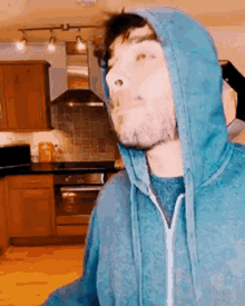 a man in a blue hoodie is making a funny face in a kitchen .