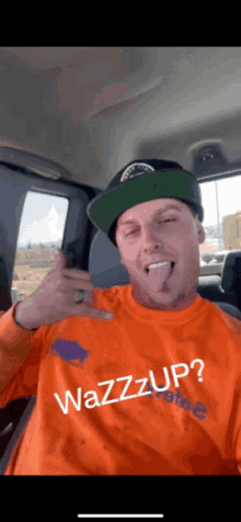 a man wearing an orange shirt that says wazzup sticking out his tongue