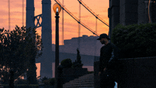 a man standing in front of a bridge with a sunset in the background