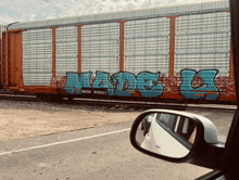 a car is reflected in the rear view mirror of a train car with graffiti on it