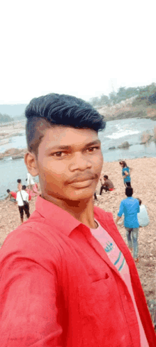 a young man in a red shirt is taking a picture of himself on the beach