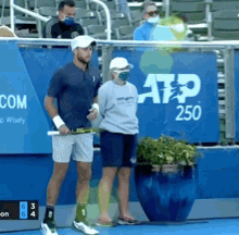 a man holding a tennis racquet stands next to a woman wearing a mask in front of an atp 250 sign