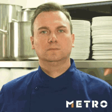 a man in a blue chef 's uniform is standing in front of stacks of white plates and pots ..