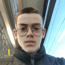 a young man wearing glasses and a black jacket is taking a selfie on a bus .