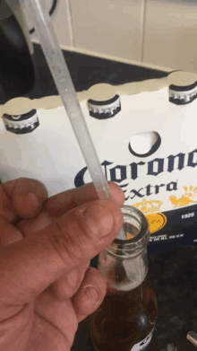 a person holding a straw in front of a pack of corona extra