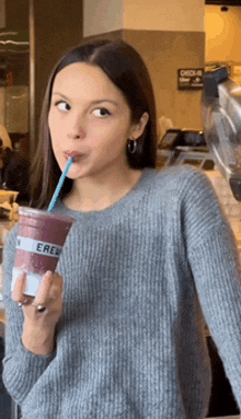 a woman in a grey sweater drinking a smoothie with a straw